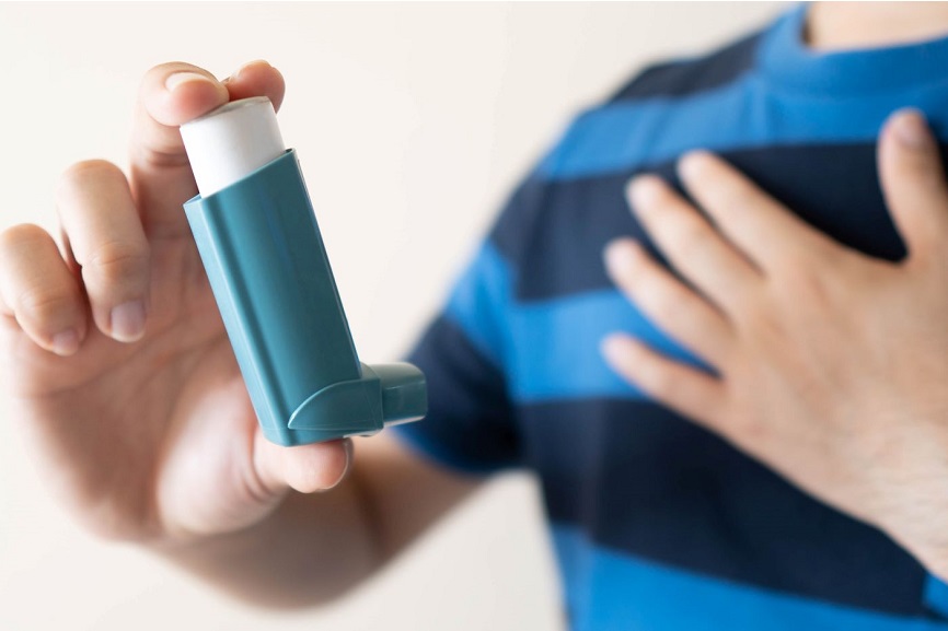 Eine Person im blauen T-Shirt hält einen Inhalator in die Kamera. 